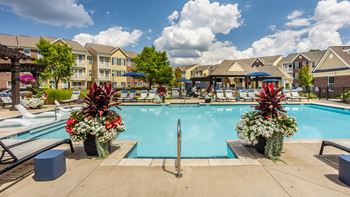 A pool surrounded by flowers and chairs with apartment buildings in the background